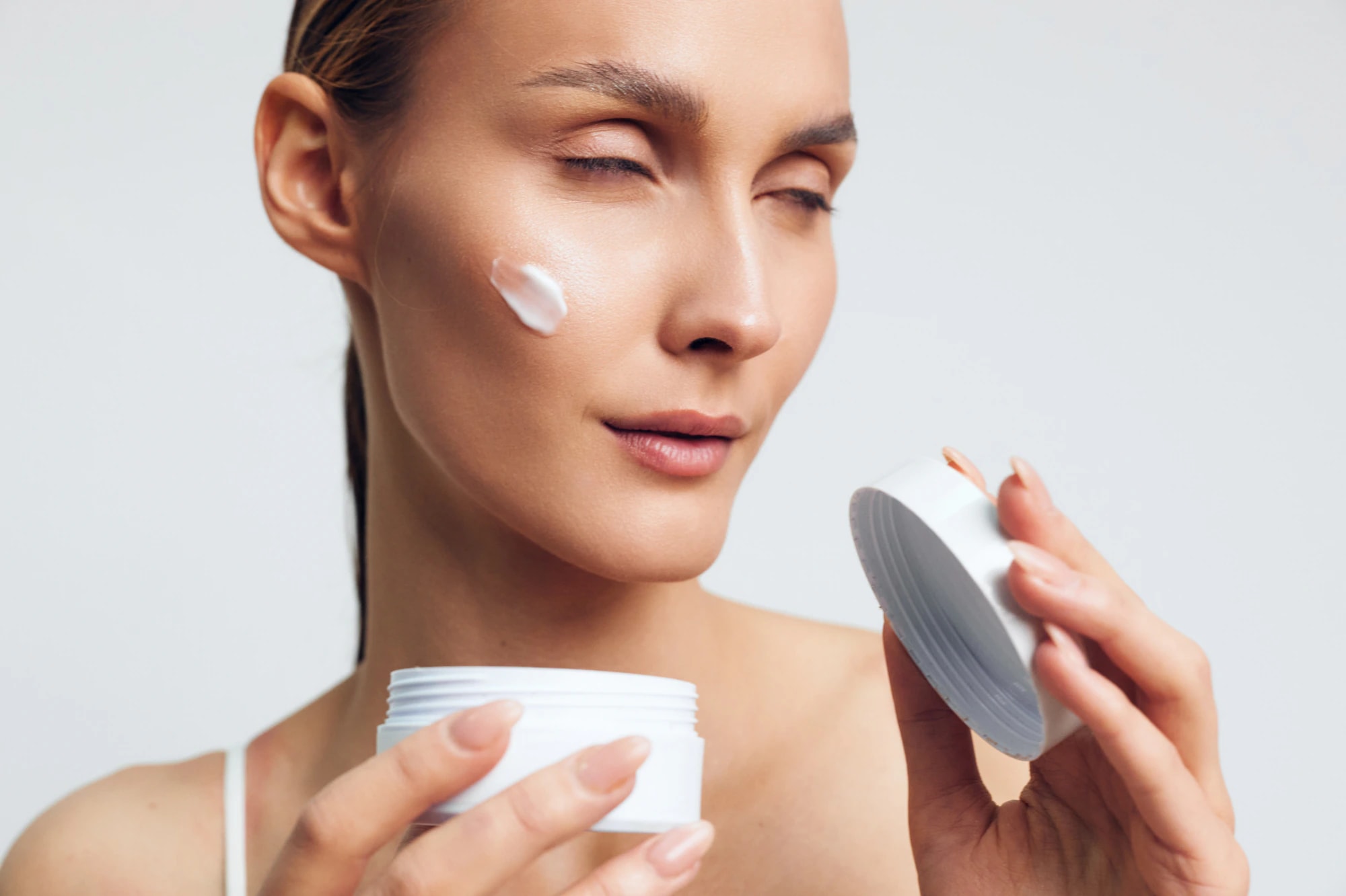 A woman applying moisturizer to her cheek as part of an aftercare routine.